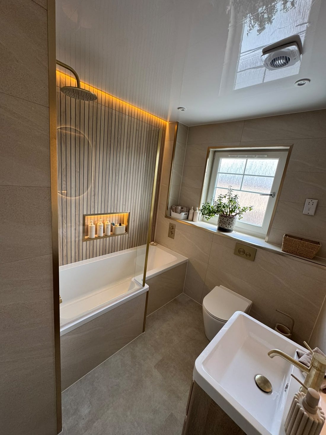 Cove-lit bathroom renovation in Glasgow with panelled wall, gold shower screen and lit niche