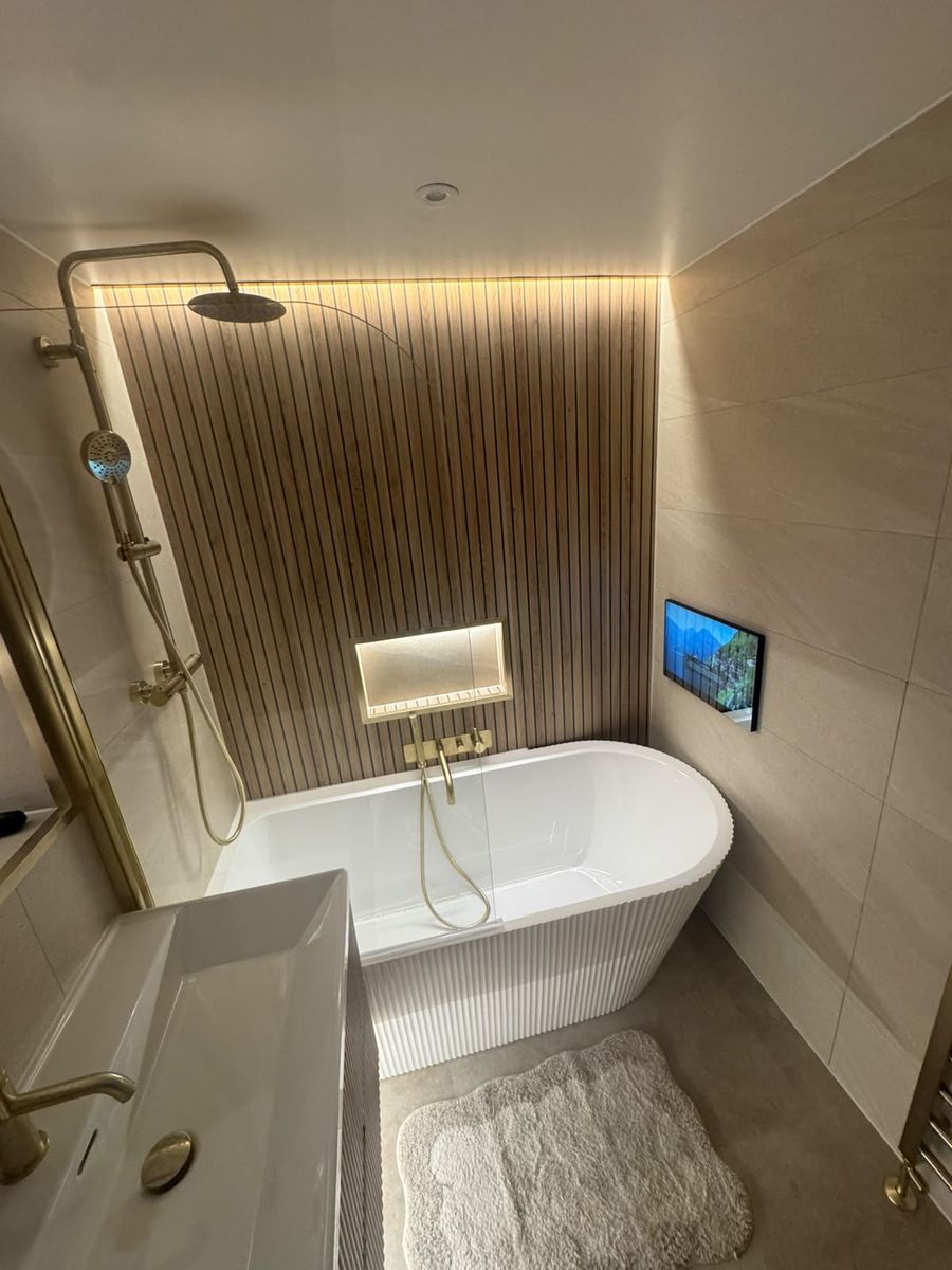 Bathroom TV set into tiled wall beside panelled bath